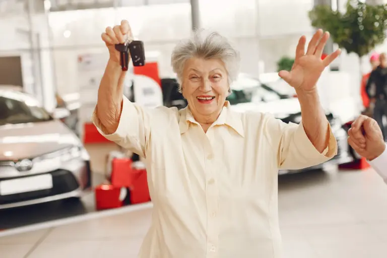 Idosa sorrindo mostrando a chave de um carro novo em uma concessionária